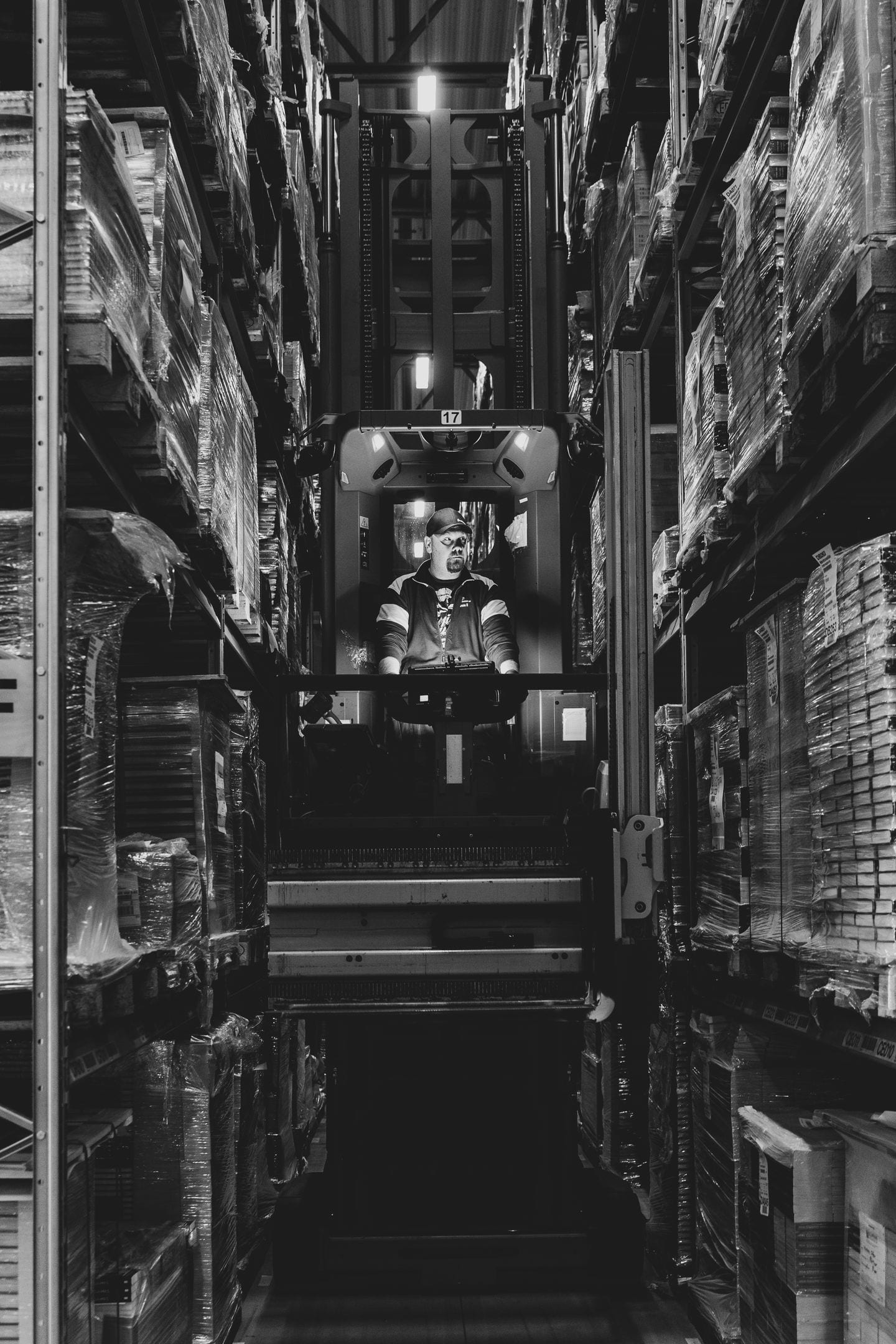 Warehouse operator driving a forklift between stocked shelves.