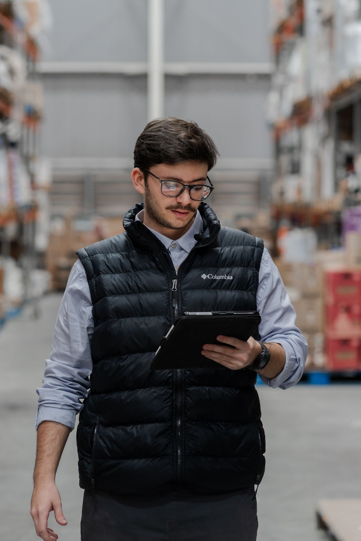 Warehouse worker checking inventory on a tablet among stored goods.