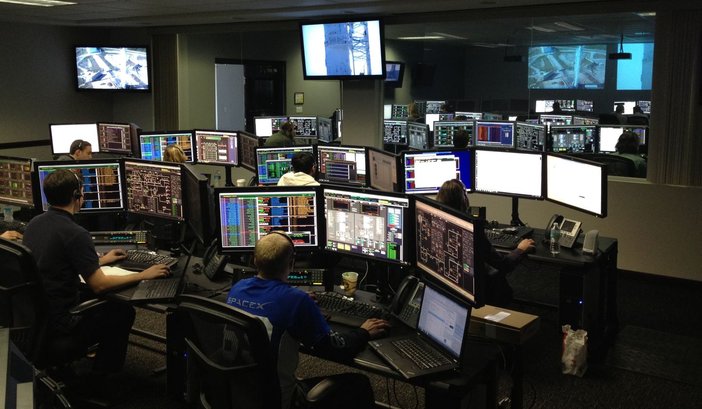 Technical team working at multiple computer monitors in a control room.